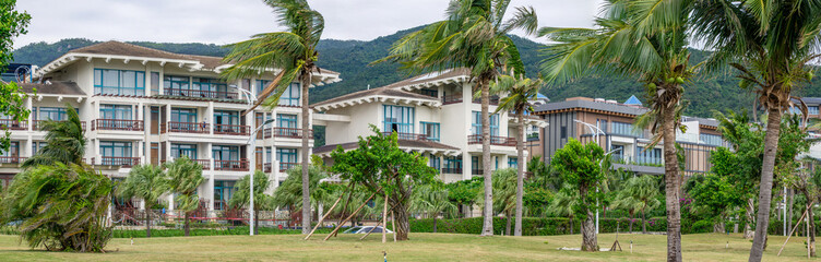 Luxury villas and hotels in Sanya Bay on Hainan Island, low-rise resort architecture surrounded by tropical palm trees and green mountains, concept of elite leisure and real estate in China.