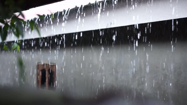 Heavy rain falling from roof eaves of urban residential house during rainy season.