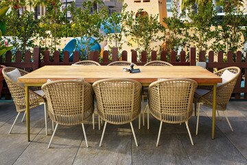Family leisure area featuring a large wooden dining table with a reserved sign and wicker chairs on a modern restaurant terrace with a playground background.