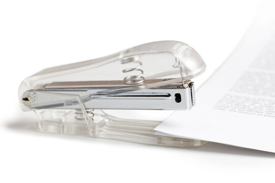 Close-up of a office stapler with matte transparent plastic handles and several sheets of paper isolated on white with shadow