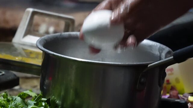 person cracking a white egg into a metal pot for remove shell