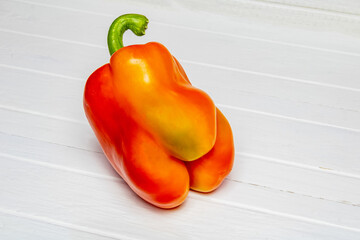 Juicy red pepper with a green tail lies on a wooden white surface 