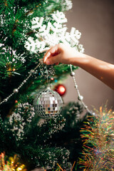 A child hangs a shiny Christmas ball, an ornament hanging from dark green branches, creates a festive atmosphere.