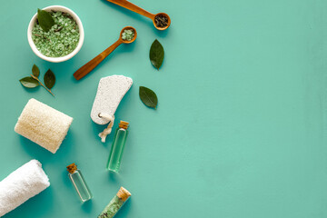 Obraz na płótnie Canvas Homemade organic cosmetics products - tea tree essential oil and sea salt in mortar and pestle with green leaves on green background, top view