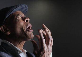 man praying to god with hands together portrait view of Caribbean man praying with black background...