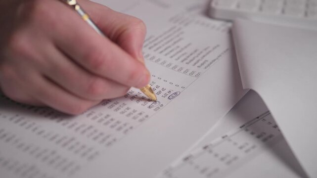 Hand Annotating Expense Report Among Papers, Office Worker Marking Totals And Attaching Sheets, Folded Printouts And Calculator Edge Visible, Organized Filing And Careful Number Checking