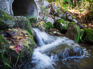 A trickle of water from a concrete pipe into nature