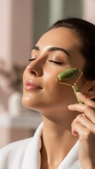 Woman in white robe using jade roller on her face for skincare in a serene setting.