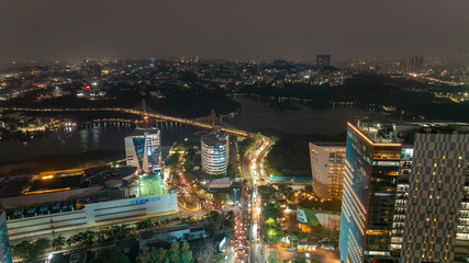 Aerial view of the vibrant Durgam Cheruvu bridge illuminated over the tranquil lake waters amid the bustling cityscape at night, Hyderabad, Telangana, India.