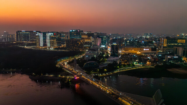 Aerial view of the illuminated Durgam Cheruvu bridge stretching across the tranquil waters, reflecting the vibrant cityscape against the dusky horizon, Hyderabad, Telangana, India.