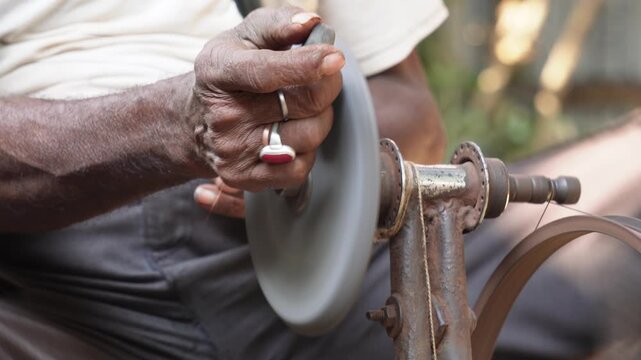 person using a traditional, pedal-operated grinding machine to sharpen a knife.