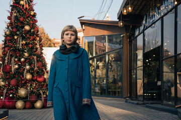 Teen girl walking in festive snowless city street decorated for Christmas