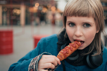 Happy teenage girl bites Corn dog at festival street fair