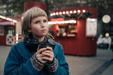 Teen age girl with paper cup of hot drink walking at holiday street fair