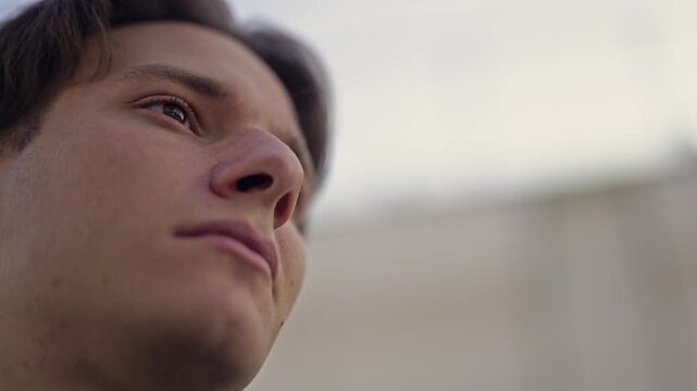 A thoughtful young man gazes upwards with a serious and determined expression, envisioning future success and contemplating important business decisions.