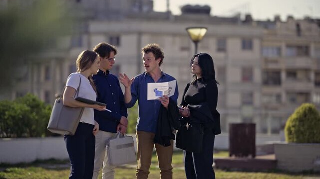 A dynamic group of young business professionals engages in an outdoor discussion, exchanging innovative ideas and reviewing project documents.
