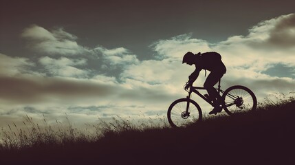 Fototapeta premium Silhouette of a mountain biker riding uphill against a dramatic cloudy sky.
