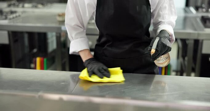 Chef, cleaning and hands with cloth, kitchen and sanitation with chemical or maintenance of surface. Wiping, workstation and person with spray for disinfection, hygiene and food safety in restaurant
