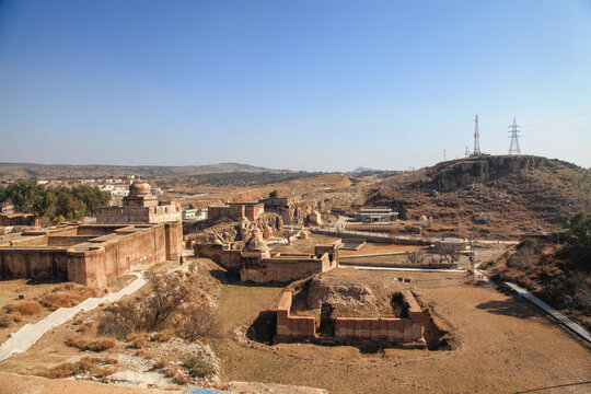 View of ancient sandstone structures scattered across the arid landscape under a clear blue sky, contrasting with the rugged terrain, Katas, Punjab, Pakistan.