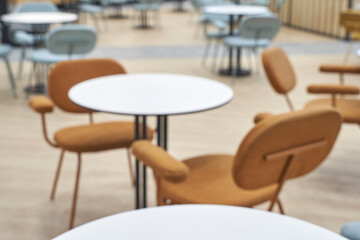Blurred modern cafe interior with brown chairs and white tables in a bright contemporary setting.