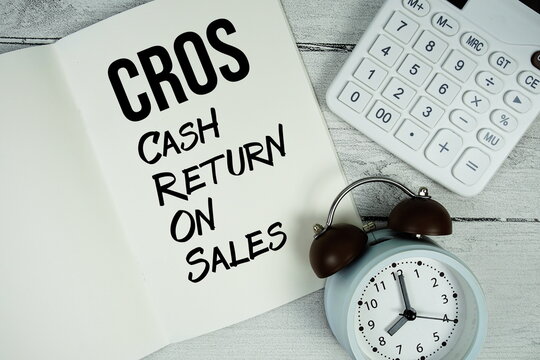 CROS Cash Return On Sales text on paper notebook page with alarm clock and calculator on wooden background