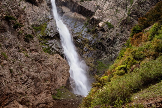 View of a powerful waterfall cascades down rugged cliffs, contrasting with vibrant green vegetation in the mountain, Kalam, Khyber Pakhtunkhwa, Pakistan.