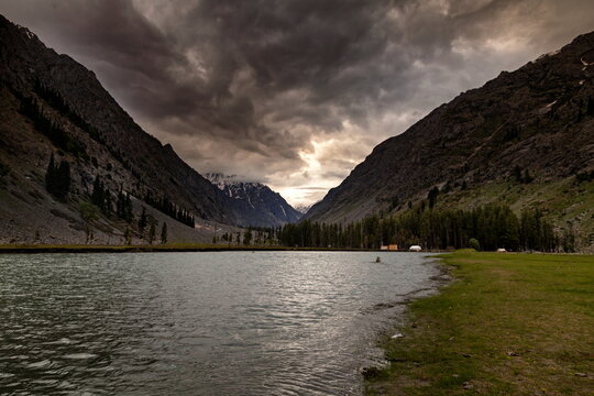 View of the still lake reflecting the dramatic sky and towering mountains, a serene yet powerful landscape, Kalam, Khyber Pakhtunkhwa, Pakistan.