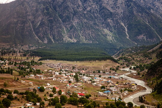 View of a vast valley where a river winds through a landscape dotted with houses, shadowed by towering mountains, Kalam, Khyber Pakhtunkhwa, Pakistan.