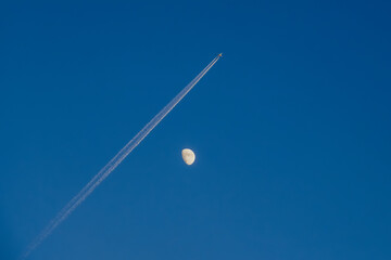 Airplane Trail Crossing the Moon in Clear Blue Sky