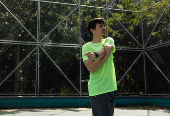 Athletic man performing a shoulder stretch with a crossed arm, pulling one arm across his body and assisting with the other hand before exercising outdoors