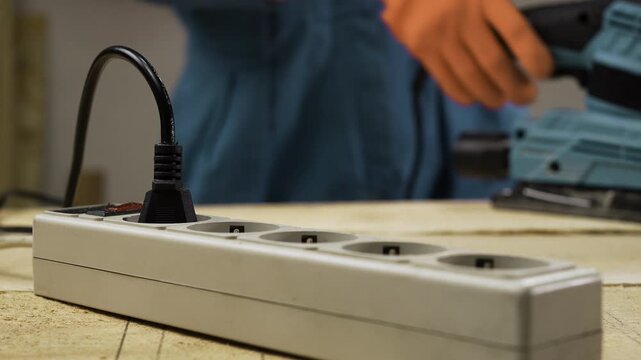 Carpenter hands plugging electric cord into power strip for sanding machine