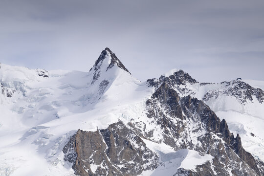 View of jagged, snow-dusted peaks pierce the serene sky, a symphony of white and grey in a breathtaking mountain panorama, Zermatt, Valais, Switzerland.