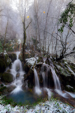 Snowy Andoin waterfalls flowing through a frozen winter forest, Long exposure water over mossy rocks
