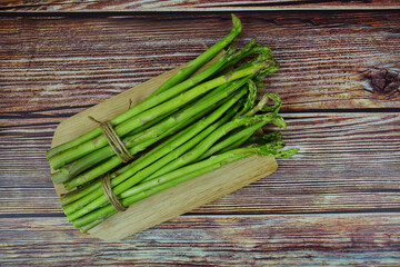 Bunch of fresh green asparagus stems with cutting wooden board on wooden background