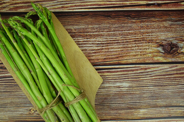 Bunch of fresh green asparagus stems with cutting wooden board on wooden background