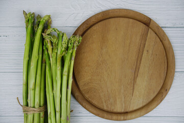 Bunch of fresh green asparagus stems with cutting wooden board on wooden background