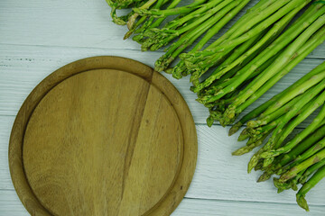 Bunch of fresh green asparagus stems with cutting wooden board on wooden background