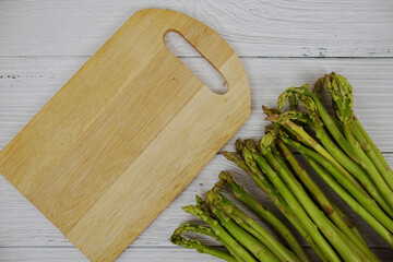 Bunch of fresh green asparagus stems with cutting wooden board on wooden background