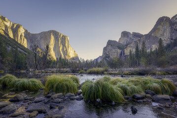 View of golden light kissing the granite faces of El Capitan and Half Dome, reflected in the Merced River flowing through the valley, Yosemite Valley, California, United States.