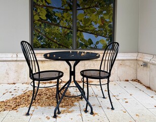 Quaint outdoor black bistro sidewalk seating with a table and two chairs with fall leaves
