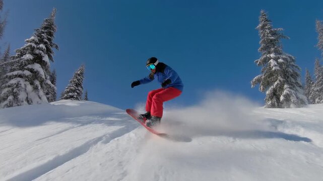 Dynamic snowboarder performing a mid-air jump on a snowy mountain under a bright blue sky