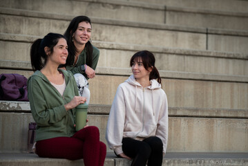 Group of women in sportswear sitting on concrete stairs, chatting happily after exercise