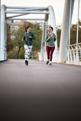 Two women running together on a bridge, embracing a healthy lifestyle and active exercise, vertical...