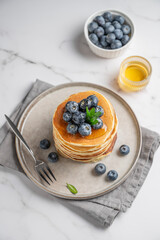 Delicious pancakes and fresh blueberries drizzled with sweet sauce on a plate on a white marble background