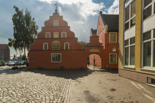 View of a vibrant red building with unique architecture stands proudly on cobblestone, a portal to history under a bright sky, Stralsund, Mecklenburg-Vorpommern, Germany.