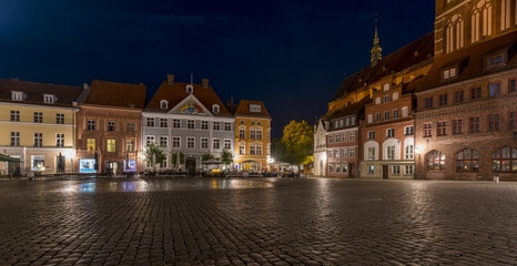 View of the old market square glows under the night sky, cobblestone reflecting light back onto the colorful buildings, Stralsund, Mecklenburg-Vorpommern, Germany.
