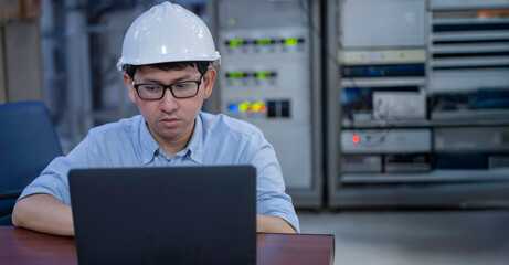 Asian male engineer wearing hardhat coding on laptop in industrial office. Professional technician...