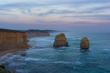 View of dramatic limestone stacks rise majestically from the turquoise sea under a pastel sky, framed by rugged cliffs, Twelve Apostles, Victoria, Australia.