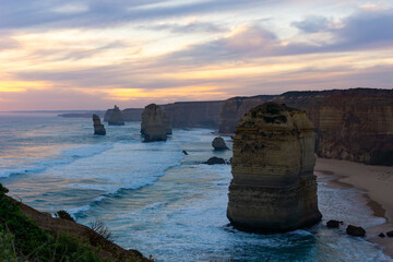 View of towering limestone stacks rise majestically from the turquoise ocean under a pastel sky, sculpted by time and tide, Twelve Apostles, Victoria, Australia.