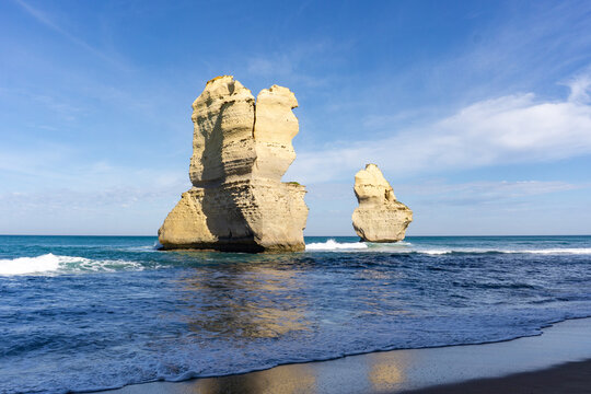 View of colossal limestone stacks rising from the turquoise sea, waves gently caressing the shore under a bright blue sky, Twelve Apostles, Victoria, Australia.